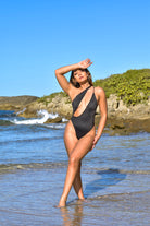 Black One-piece swimwear by Jglam Beachwear modeled on a beach.